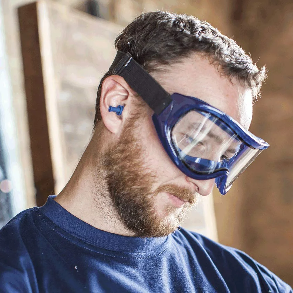 A man in a navy sweatshirt with a blue ear plug in his ear and a clear goggle with a blue frame and black strap